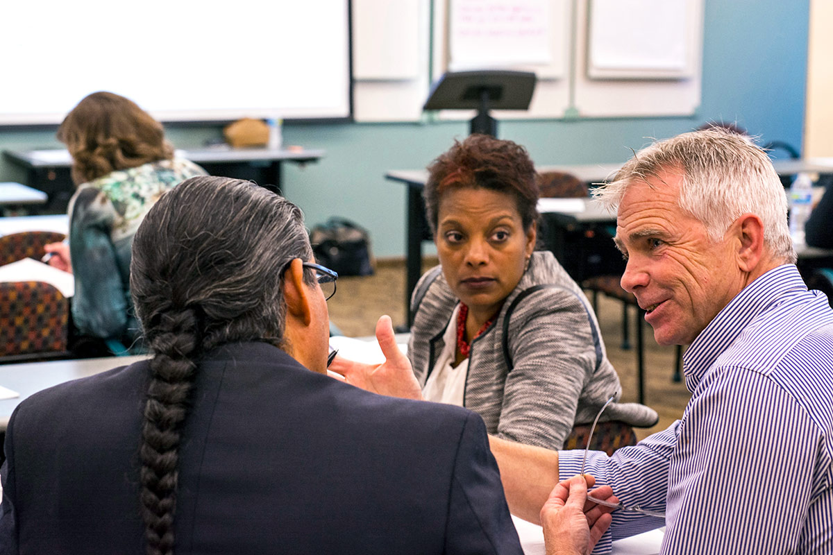 Three people engage in conversation inside a classroom. Courtesy of City Alive