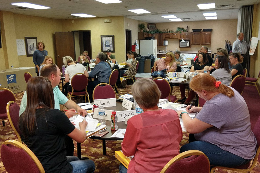 Five tables full of participants listen to a facilitator give direction during a NetWork Kansas E-Community Growing Rural Businesses event.