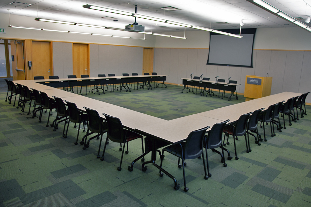A conference room featuring a U-shaped table that seats 30. A panel table with microphones and podium are at the front of the room.