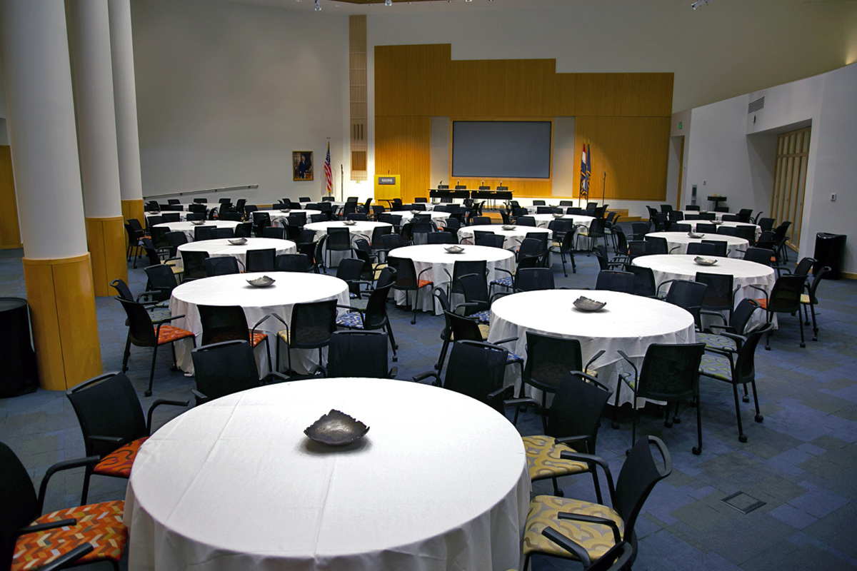 A large conference room featuring circular, cloth-covered tables which seat 200 people, and a stage with podium at the front.