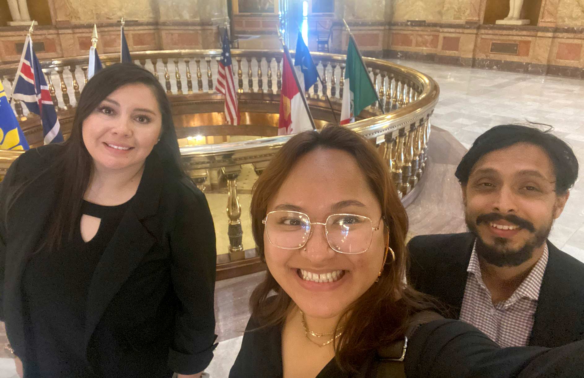 Three people pose for a selfie in front of various world flags.