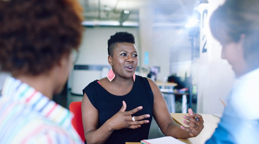 A Black entrepreneur wearing pink teardrop earrings talks with their hands.