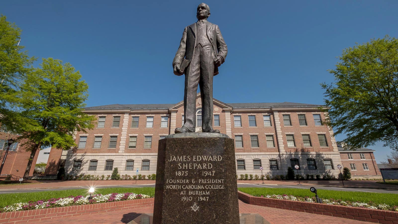 A statue of a man in front of a brick college building with an inscription that reads: "James Edward Shepard 1875-1947, Founder & President, North Carolina College at Durham 1910-1947"