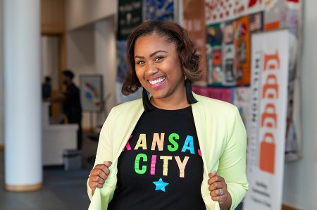 Panelist and entrepreneur India Wells-Carter poses for a photo, wearing a lime green jacket and a black t-shirt that reads, "Kansas City" in colorful, neon font.