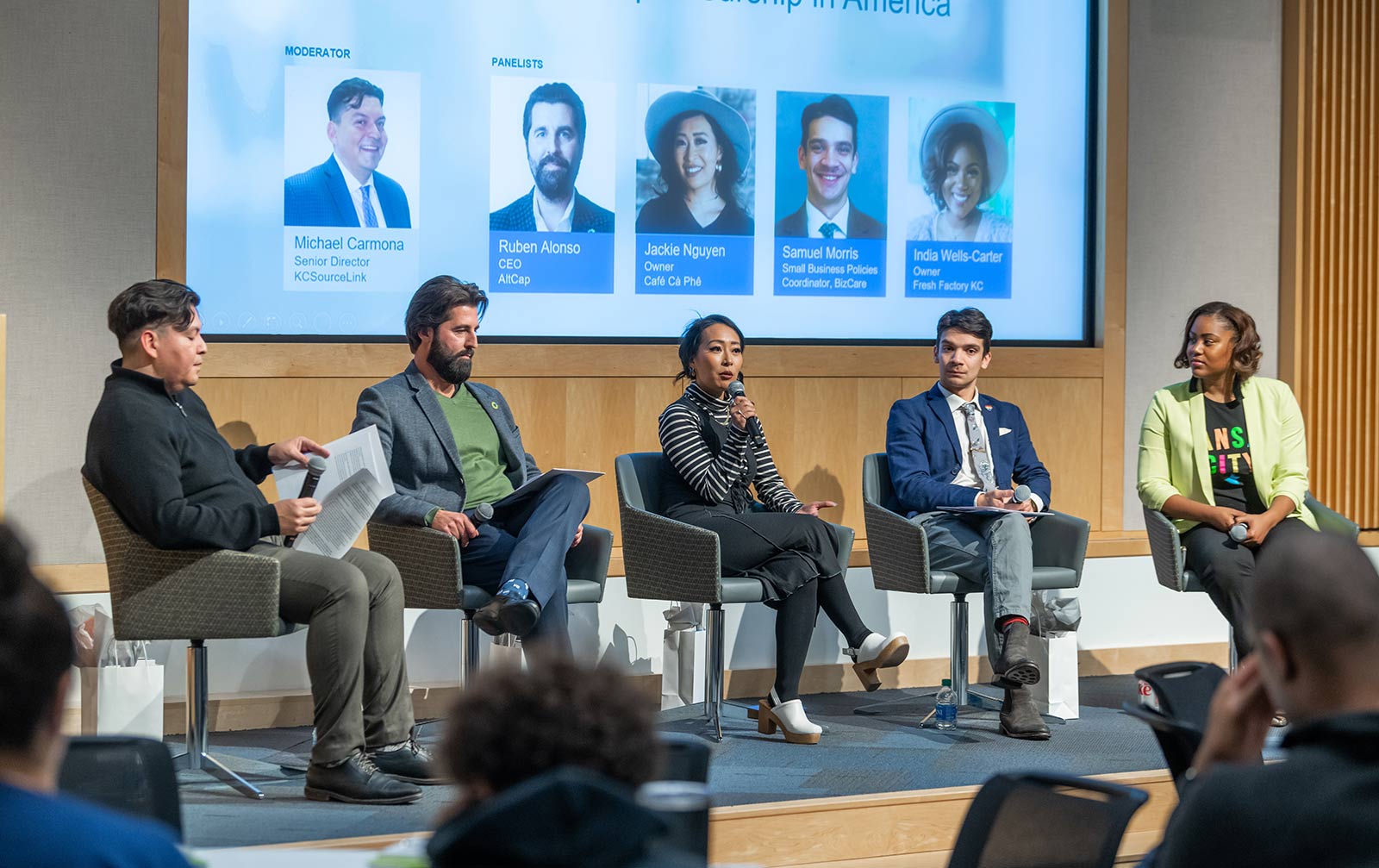 Kansas City entrepreneurs sit on a panel on stage in front of a live audience. From left to right: Michael Carmona, Ruben Alonso, Jackie Nguyen, Samuel Morris, and India Wells-Carter.