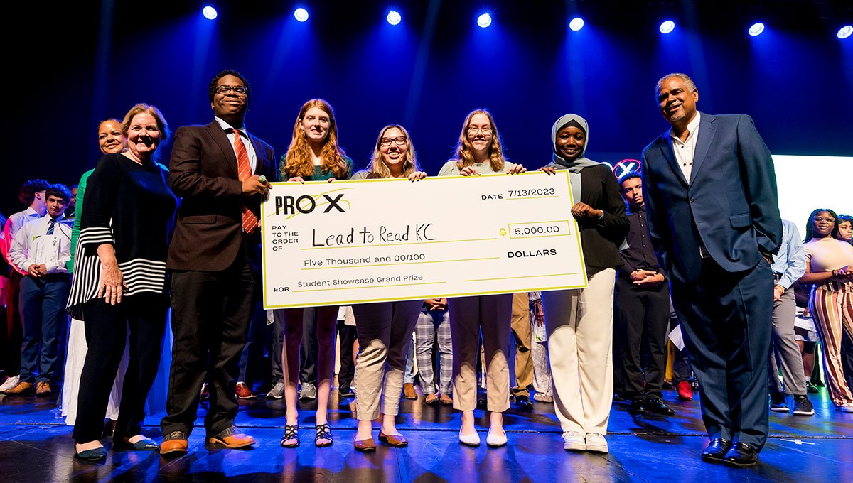 ProX students stand on a stage holding an oversized check made out to Lead to Read for $5,000 grand prize.